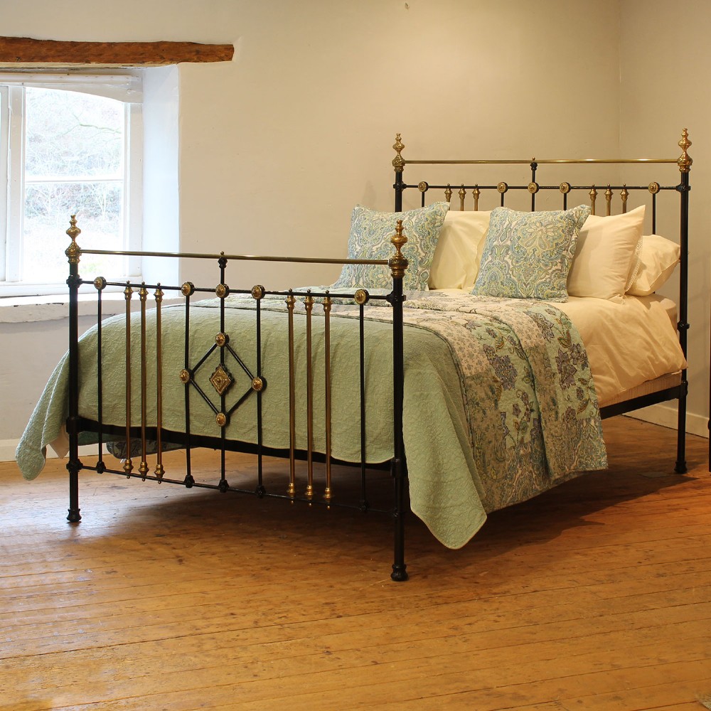 A Victorian black painted cast iron and brass king-size bedstead featuring turned brass finials, vertical spindles, and a central brass diamond motif.