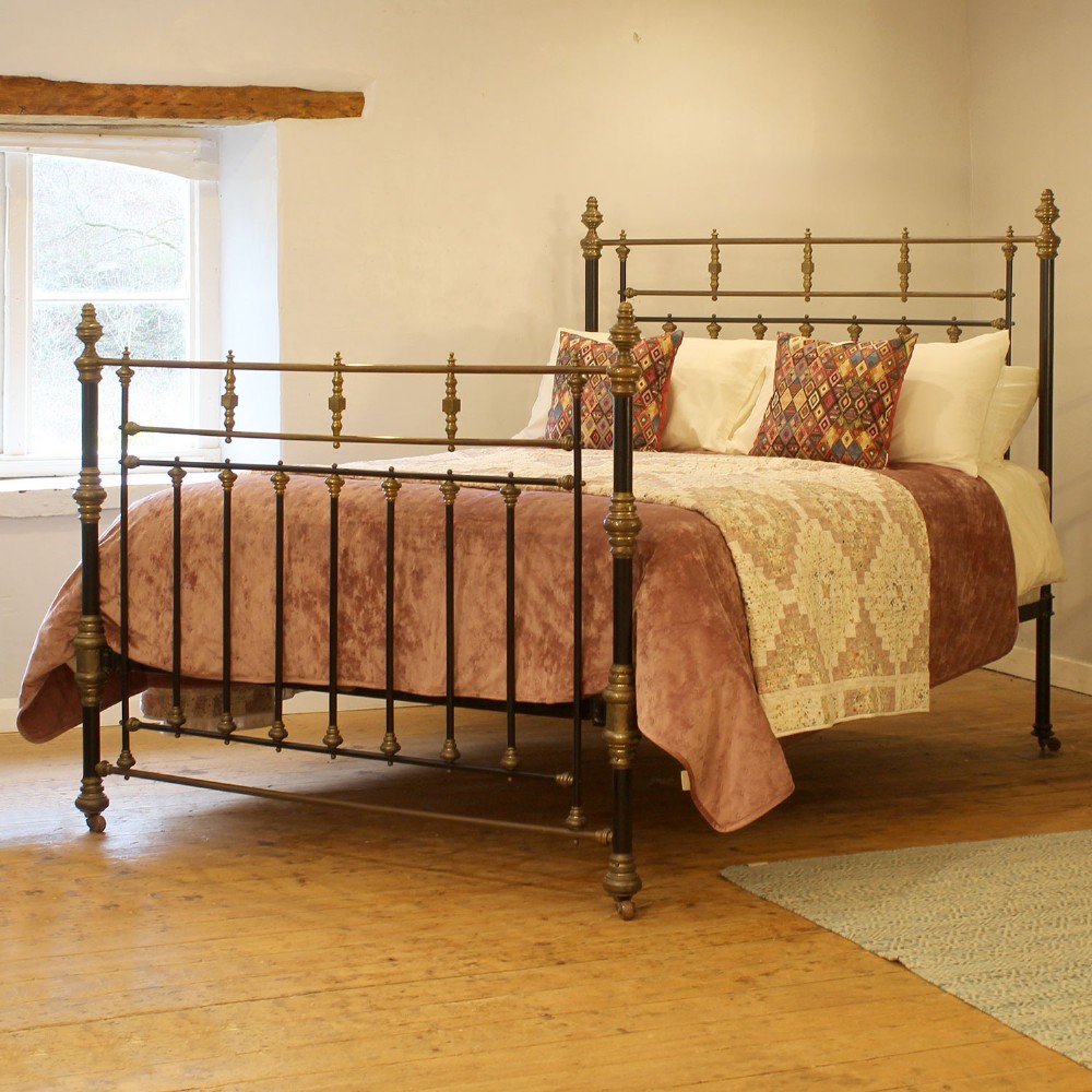 An antique king size bedstead featuring black painted iron vertical spindles topped with decorative brass rails, turned collars, and corner finials.