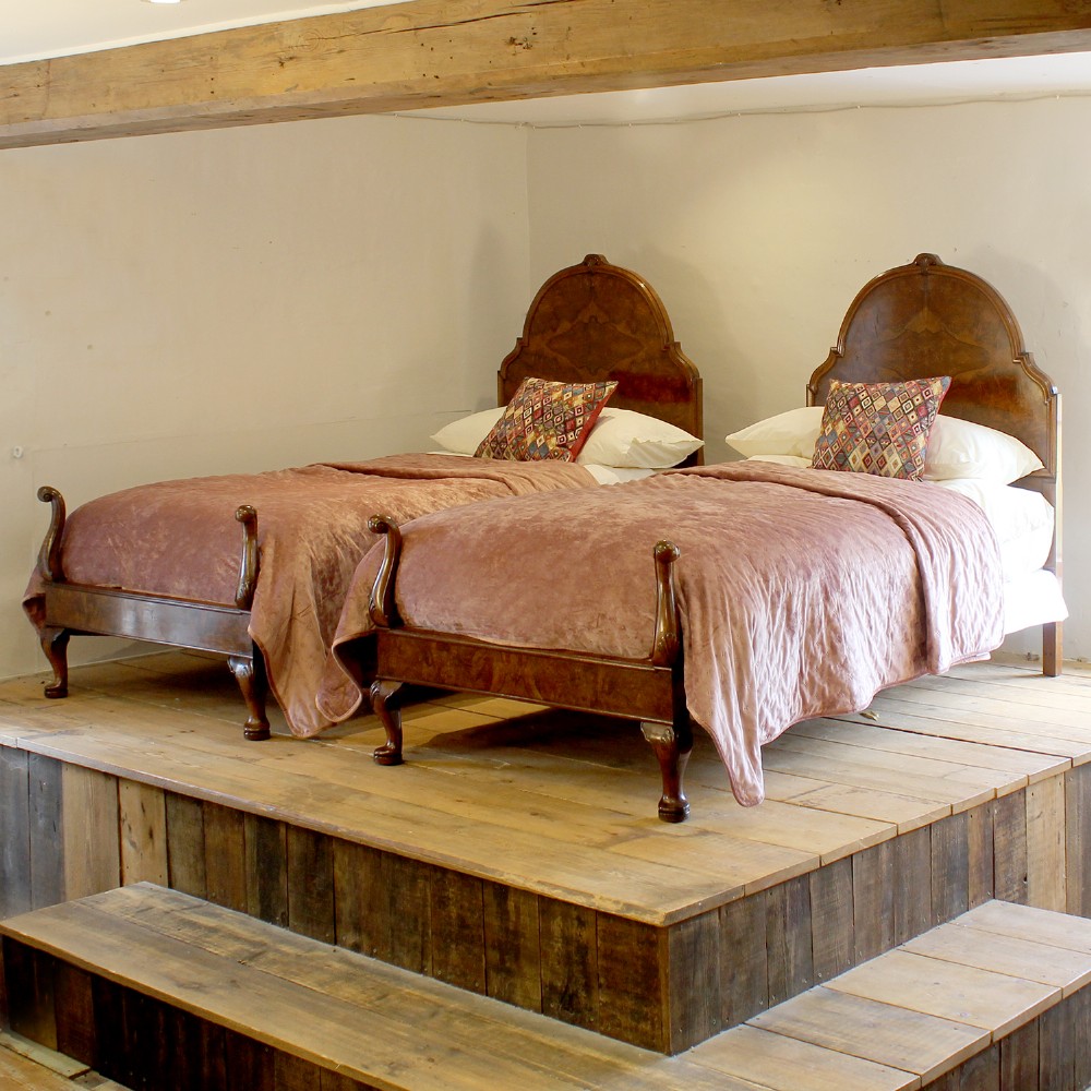 A matching pair of Queen Anne style bed frames crafted from warm brown burr walnut with arched headboards and cabriole legs.