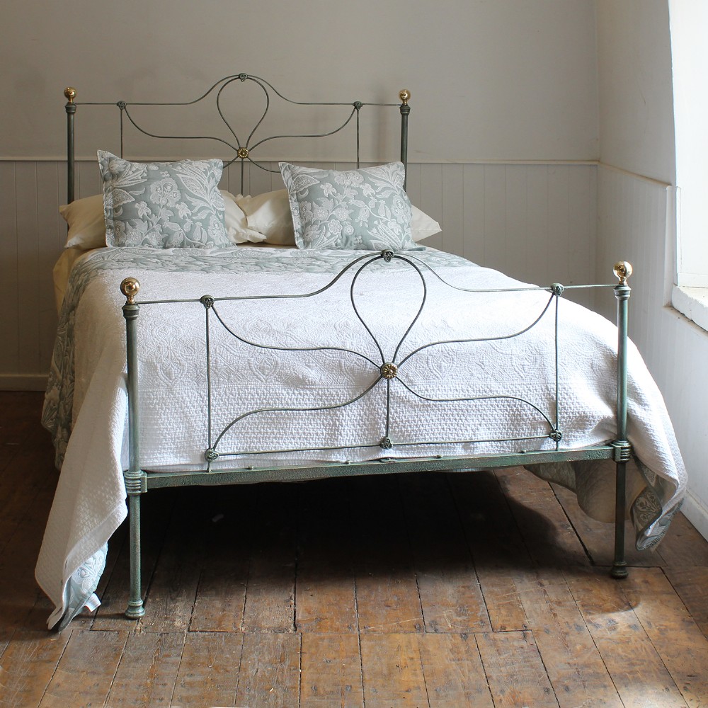 An antique double cast iron bedstead featuring a green verdigris finish, looped wirework panels, and brass finials.