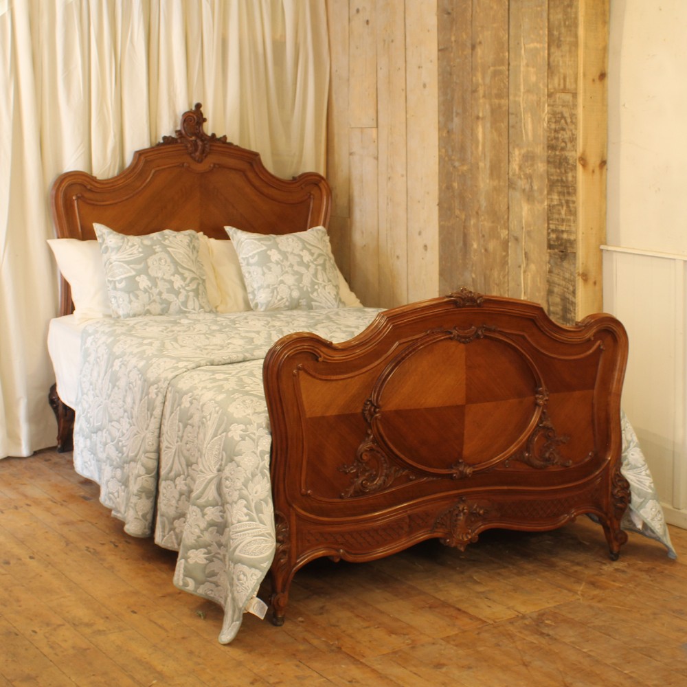 A carved walnut double bed frame featuring an arched headboard and footboard with book-matched veneers and Rococo cresting.
