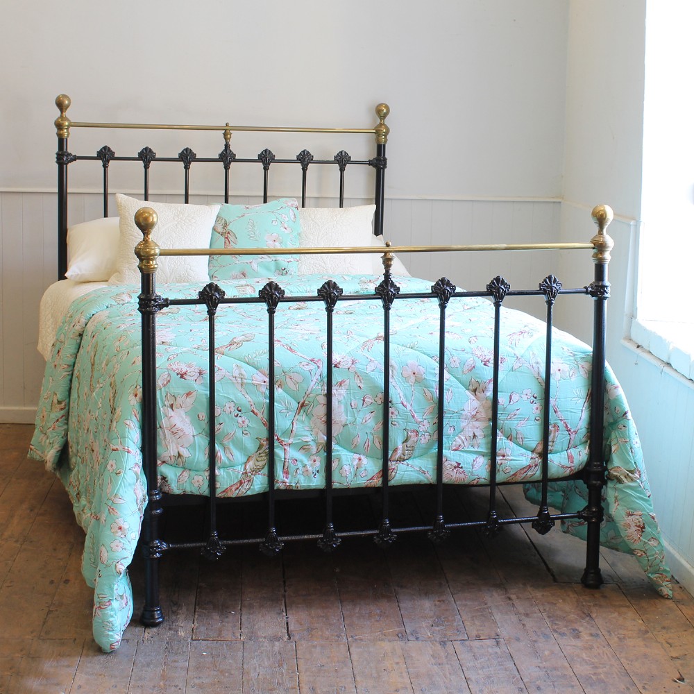 A Victorian black cast iron double bed frame featuring brass top rails, brass corner finials, and vertical iron spindles with ornate cast decorative joints.