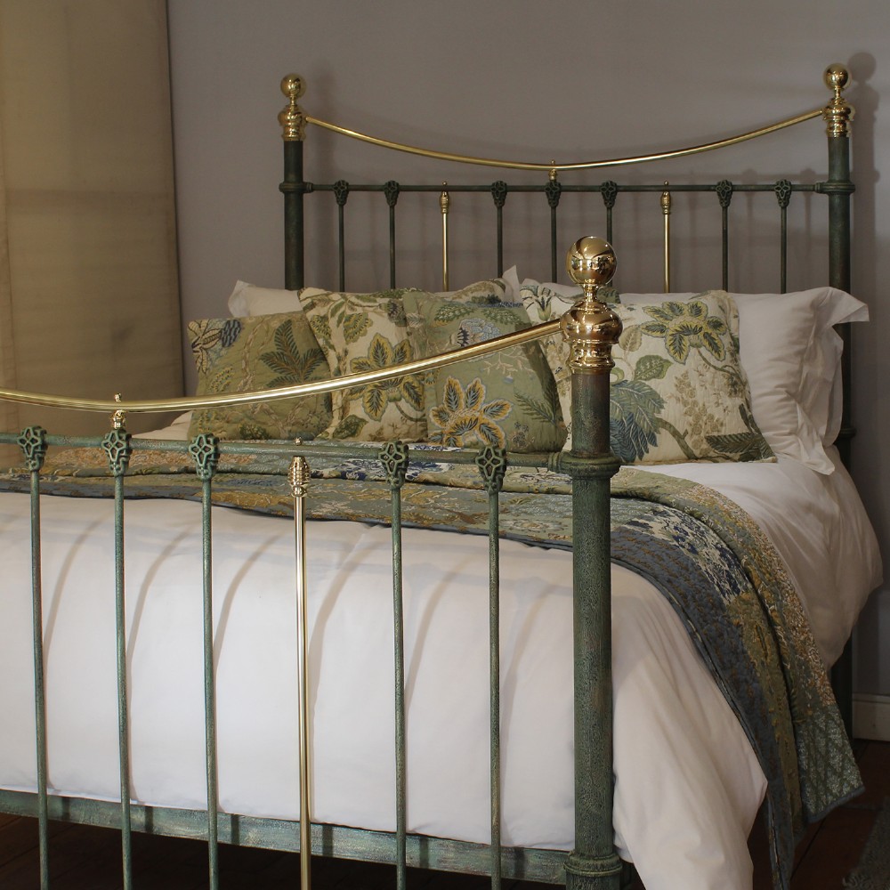 A king-size green painted metal bedstead featuring curved brass top rails, polished brass finials, and vertical central spindles. View X