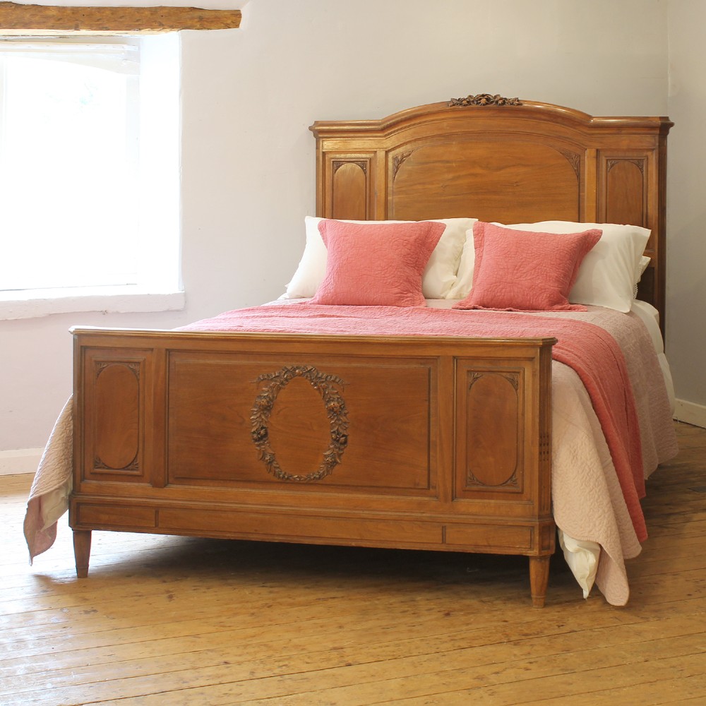 A king-size carved mahogany bed frame featuring an arched headboard and a carved floral wreath motif on the footboard.