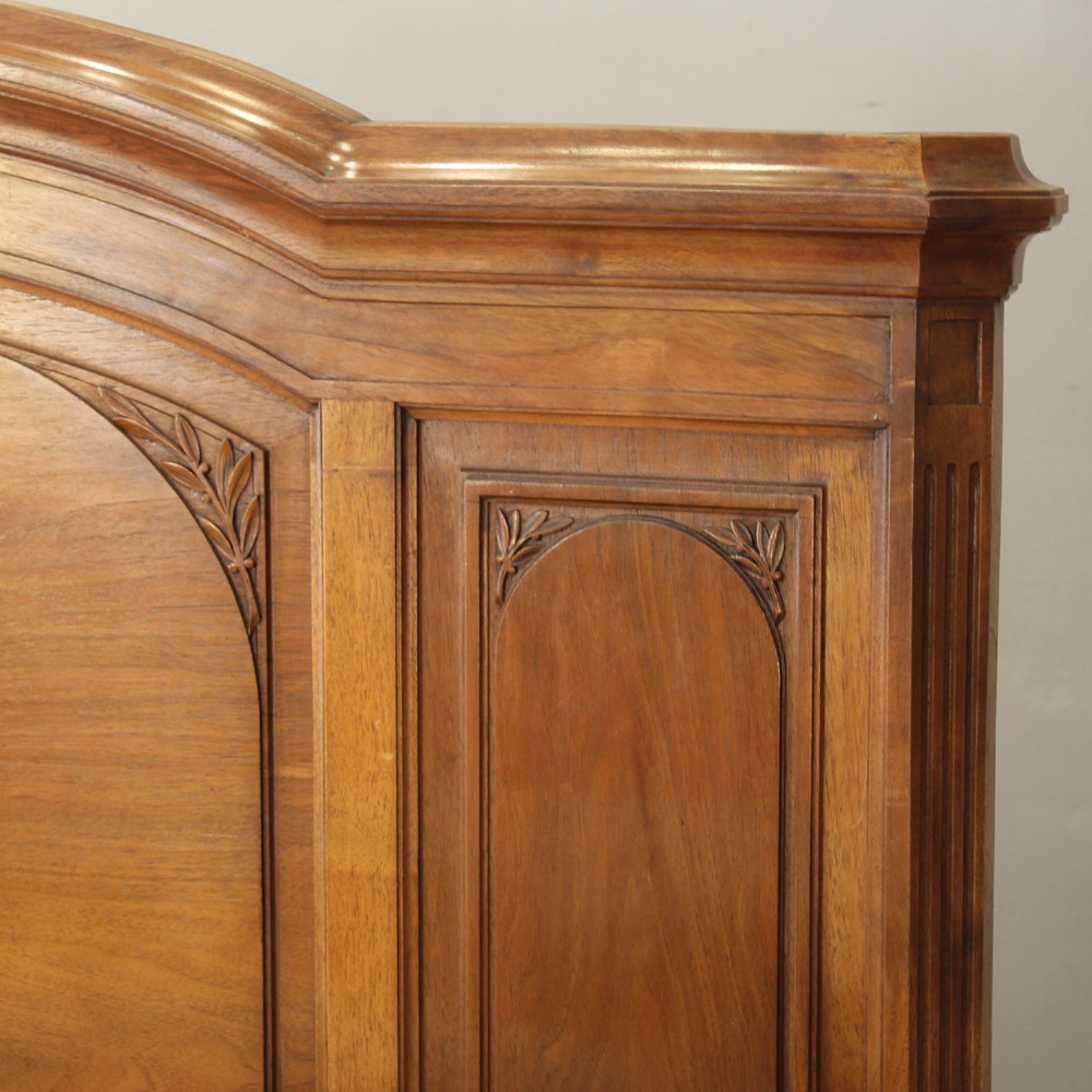 A king-size carved mahogany bed frame featuring an arched headboard and a carved floral wreath motif on the footboard. View III