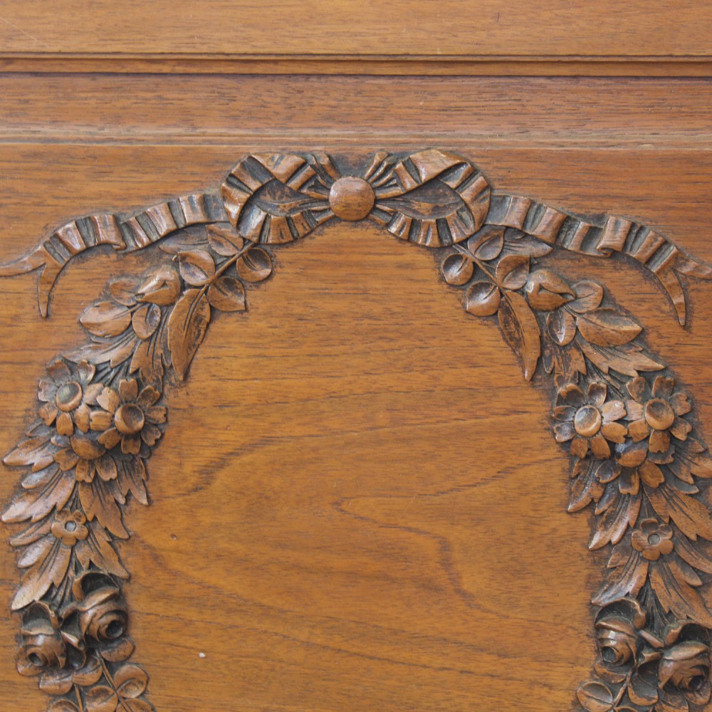 A king-size carved mahogany bed frame featuring an arched headboard and a carved floral wreath motif on the footboard. View V