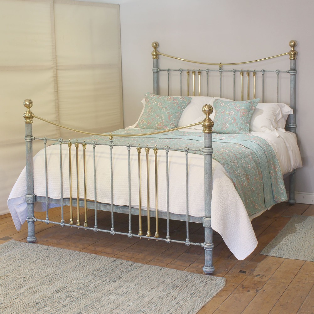 An antique king size bedstead featuring a light blue verdigris painted finish on iron spindles, accented by brass top rails and brass finials.