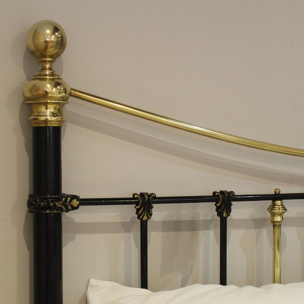 An antique Victorian black painted iron king size bedstead featuring bowed brass top rails, brass ball finials, and cast shell rosette embellishments on the footboard spindles. View IV
