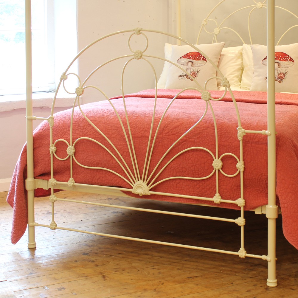 A cream-painted metal four-poster bed frame featuring an arched sunburst motif on the headboard and footboard topped with brass finials. View II