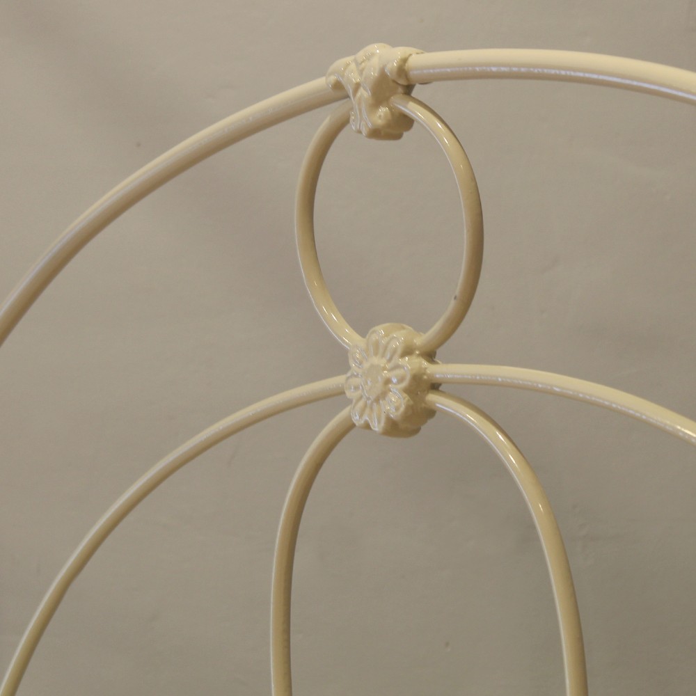 A cream-painted metal four-poster bed frame featuring an arched sunburst motif on the headboard and footboard topped with brass finials. View VIII