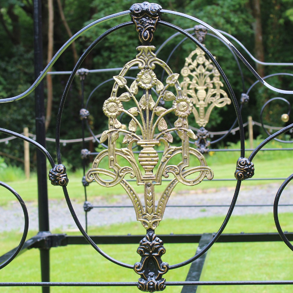 An antique black iron four-poster canopy bed frame featuring decorative scrollwork, central brass urn medallions, and brass finials. View III