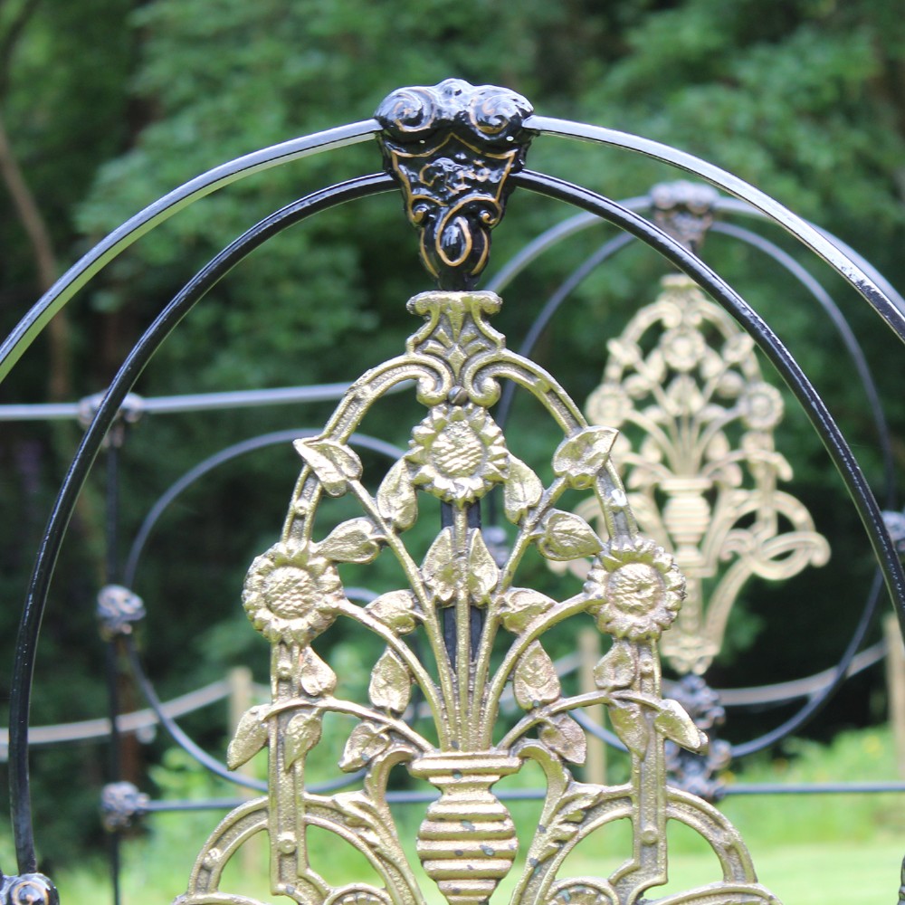 An antique black iron four-poster canopy bed frame featuring decorative scrollwork, central brass urn medallions, and brass finials. View IV