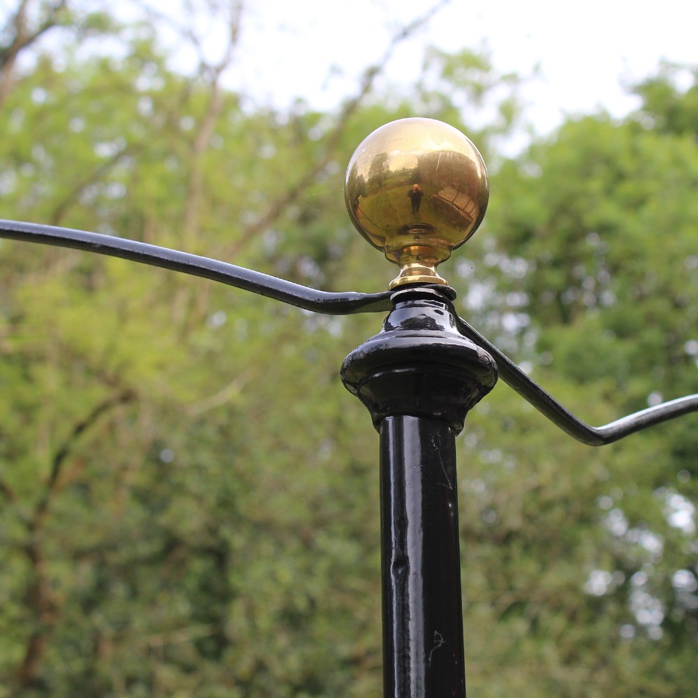 An antique black iron four-poster canopy bed frame featuring decorative scrollwork, central brass urn medallions, and brass finials. View VII