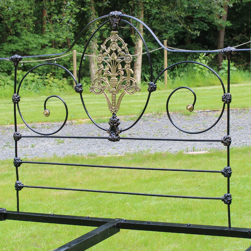 An antique black iron four-poster canopy bed frame featuring decorative scrollwork, central brass urn medallions, and brass finials. View IX