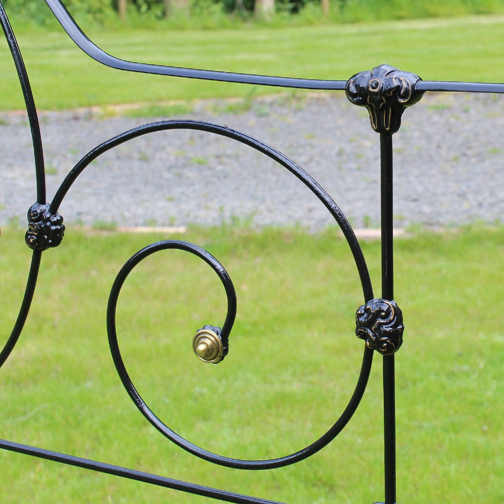 An antique black iron four-poster canopy bed frame featuring decorative scrollwork, central brass urn medallions, and brass finials. View X
