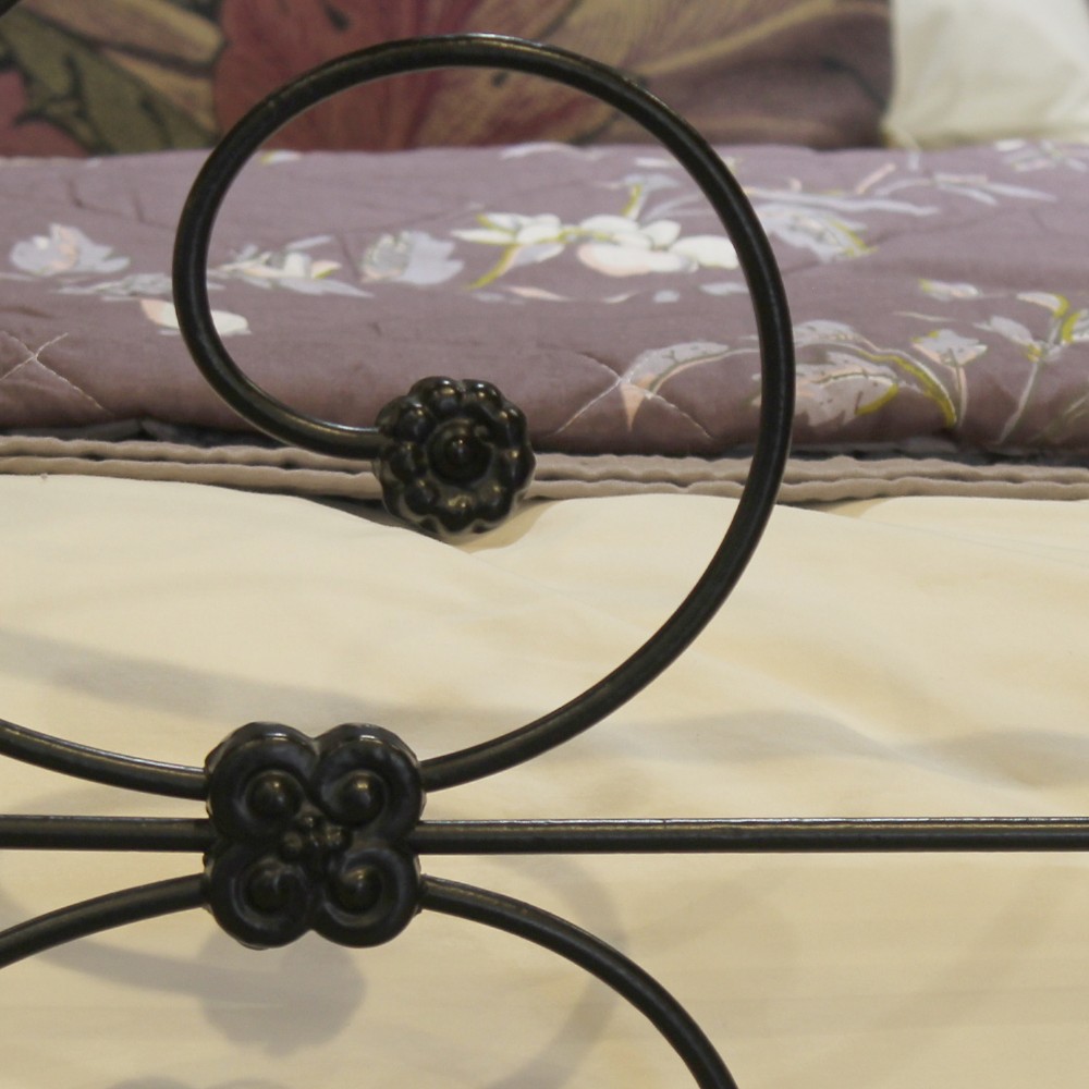 A black wrought iron king-size bed frame featuring decorative scrollwork on the headboard and footboard, topped with brass corner finials. View V