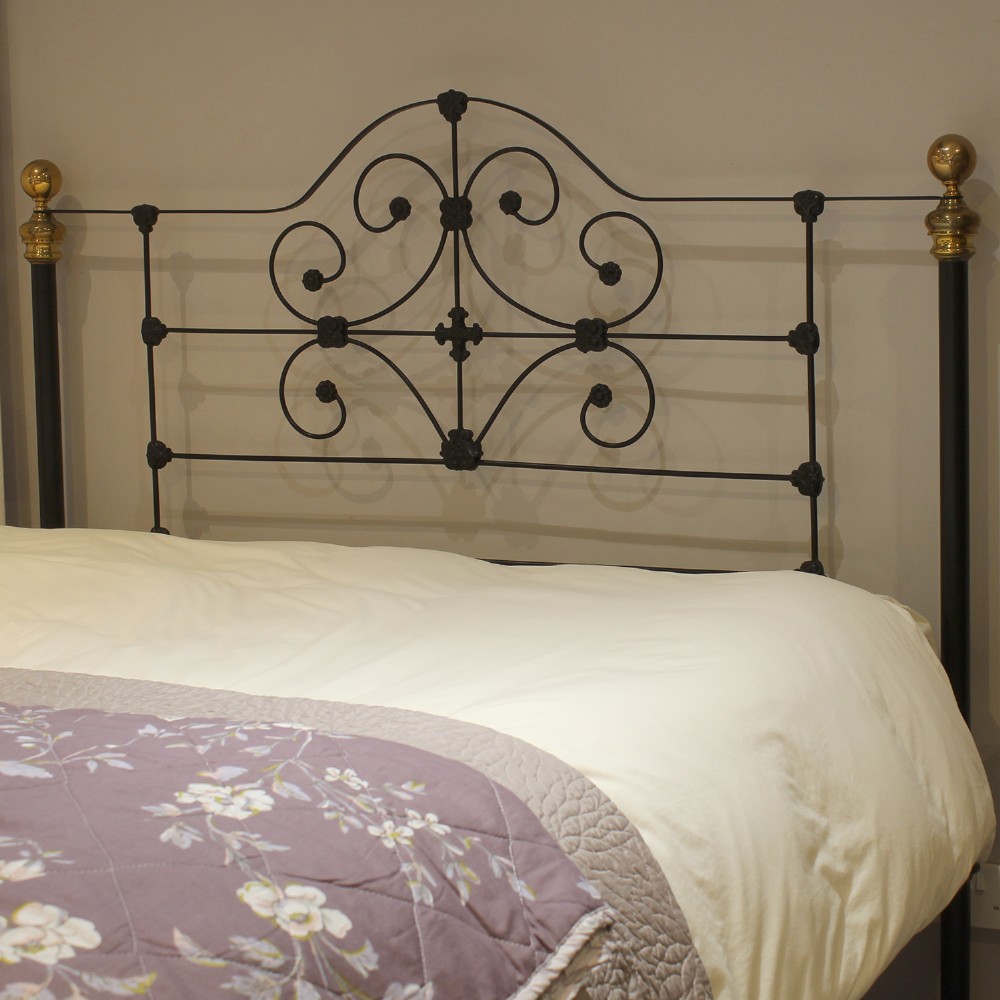 A black wrought iron king-size bed frame featuring decorative scrollwork on the headboard and footboard, topped with brass corner finials. View VI