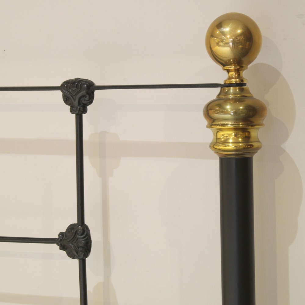 A black wrought iron king-size bed frame featuring decorative scrollwork on the headboard and footboard, topped with brass corner finials. View VII