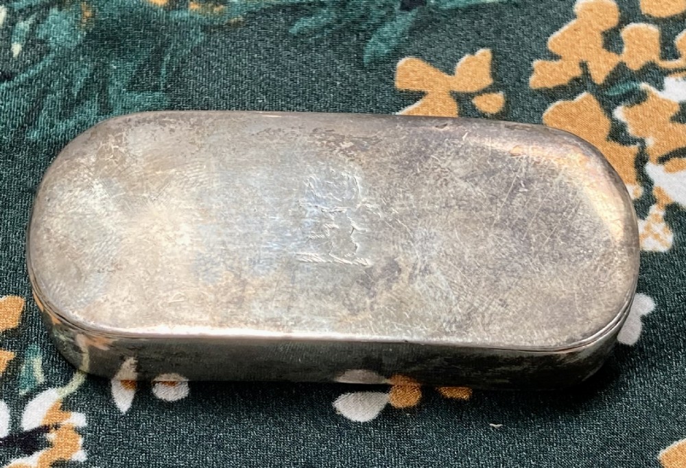 An oval Georgian sterling silver snuff box with a subtle central crest engraving and naturally aged surface patina.