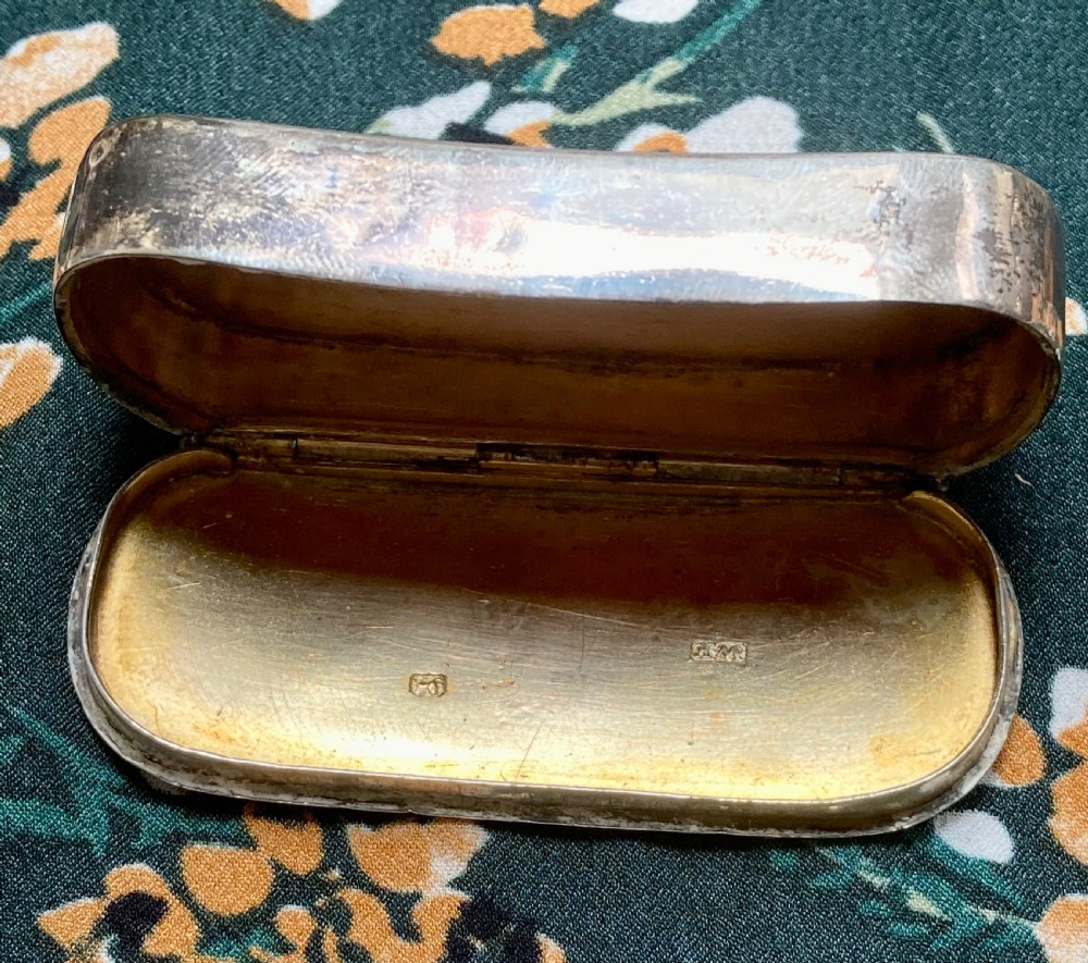 An oval Georgian sterling silver snuff box with a subtle central crest engraving and naturally aged surface patina. View III