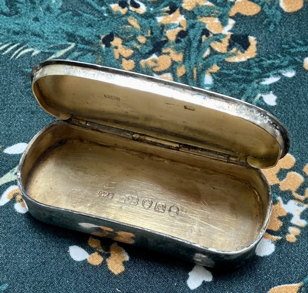 An oval Georgian sterling silver snuff box with a subtle central crest engraving and naturally aged surface patina. View IV