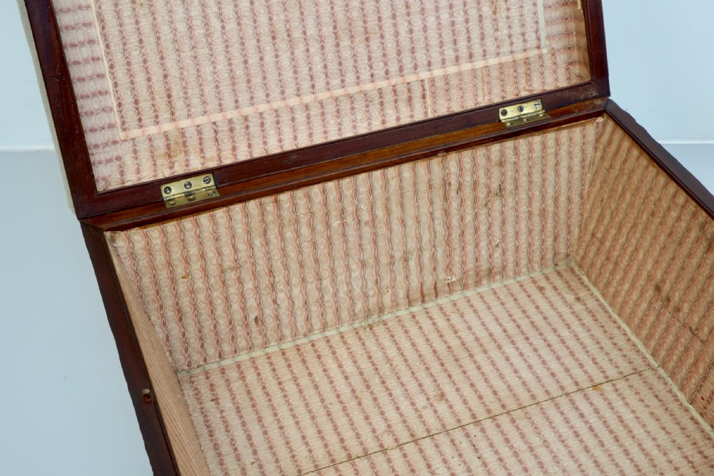 A neutral linen-upholstered antique box ottoman featuring dark wood base trim, brass stud detailing, a front keyhole, and small castors. View VIII