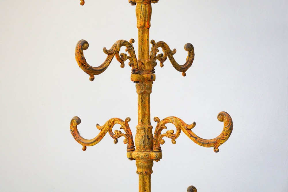 A tall, ornate yellow-painted cast iron coat stand featuring multiple tiers of scroll hooks, a twisted central column, and a hexagonal drip tray base. View IV