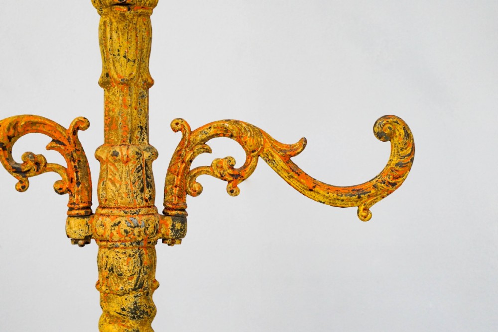 A tall, ornate yellow-painted cast iron coat stand featuring multiple tiers of scroll hooks, a twisted central column, and a hexagonal drip tray base. View V