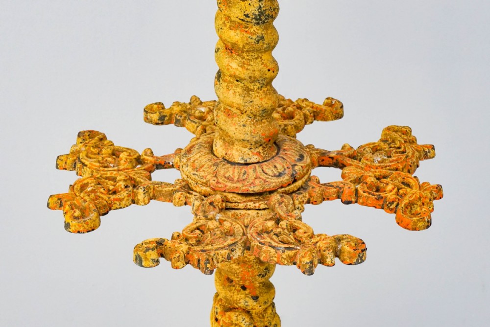 A tall, ornate yellow-painted cast iron coat stand featuring multiple tiers of scroll hooks, a twisted central column, and a hexagonal drip tray base. View VI