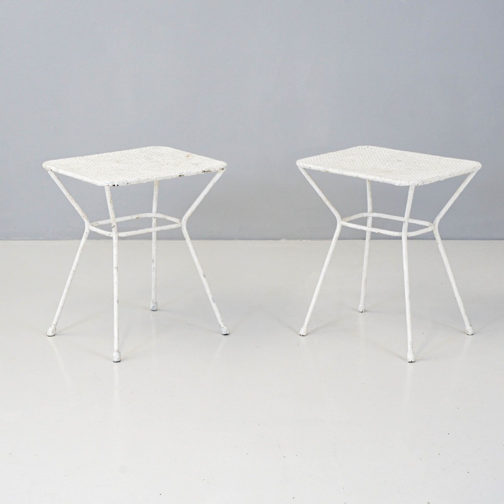 A pair of mid-century white painted metal side tables with perforated mesh rectangular tops and splayed tubular legs connected by a central circular ring.