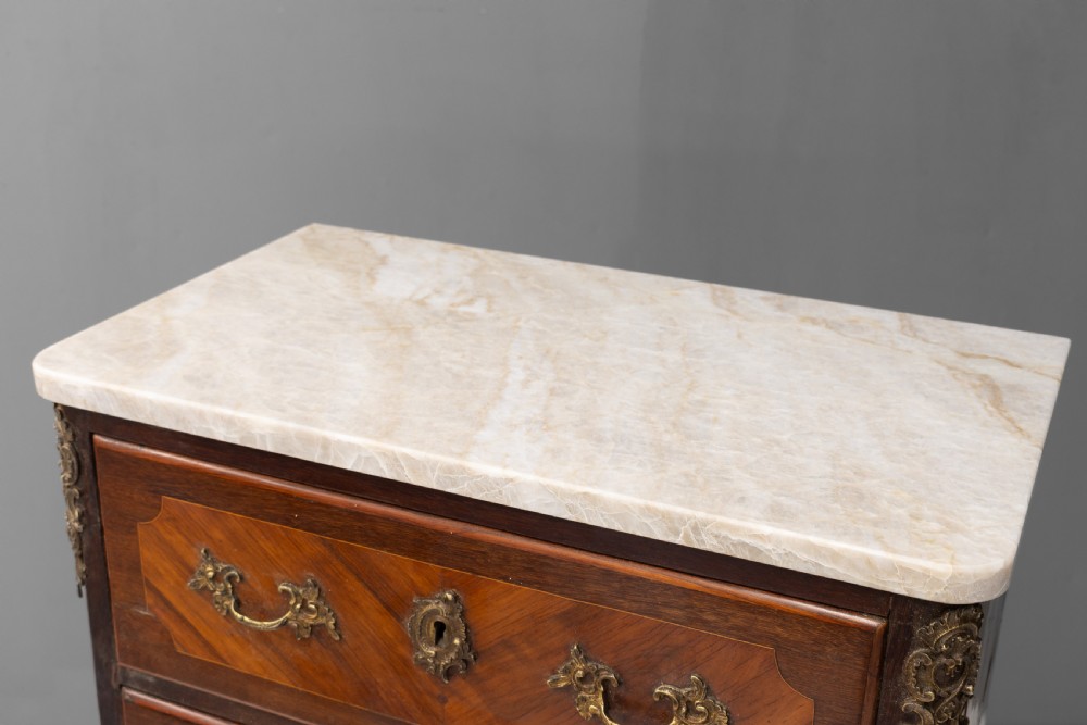 A tall, narrow French semainier chest of drawers featuring geometric wood parquetry, seven drawers, gilt bronze hardware, and a white marble top. View VI