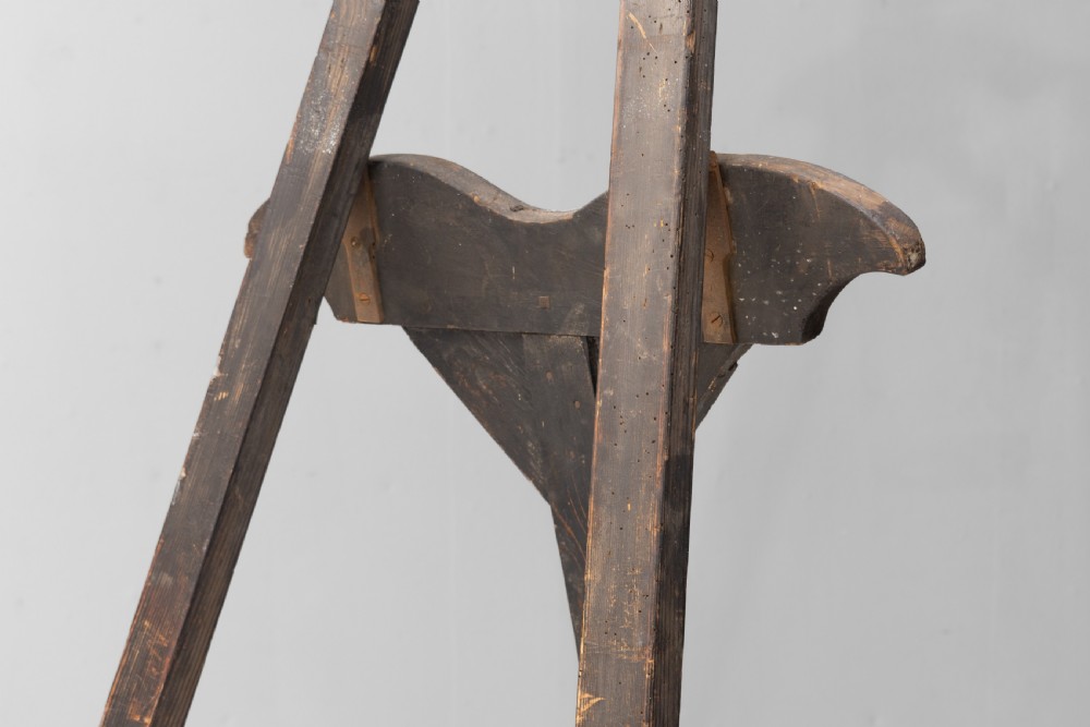 A tall, dark patinated pine A-frame studio easel featuring adjustable rest pegs and a carved decorative upper crossbar. View II
