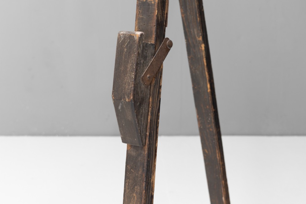 A tall, dark patinated pine A-frame studio easel featuring adjustable rest pegs and a carved decorative upper crossbar. View IV