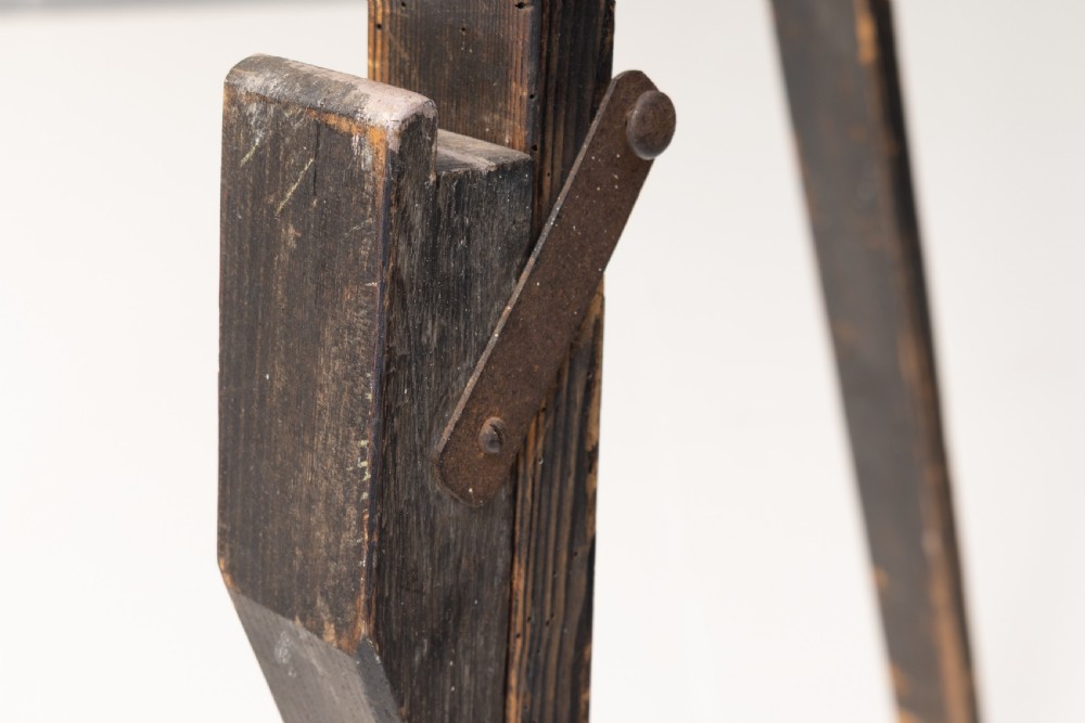 A tall, dark patinated pine A-frame studio easel featuring adjustable rest pegs and a carved decorative upper crossbar. View V