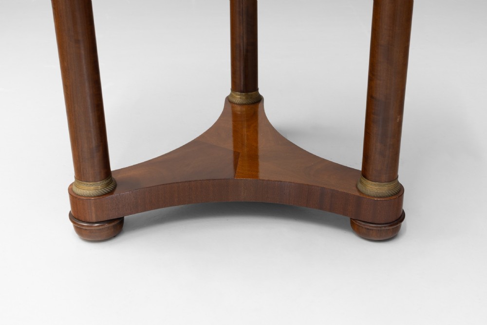 A French Empire style circular mahogany gueridon table featuring a dark marble top supported by three cylindrical columns on a tri-form base. View IV