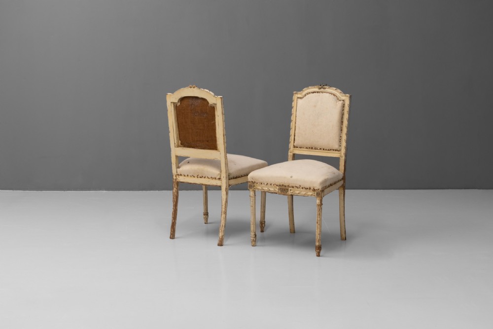 A pair of French Louis XVI style side chairs featuring distressed cream painted frames, tapered fluted legs, and neutral fabric upholstery. View II