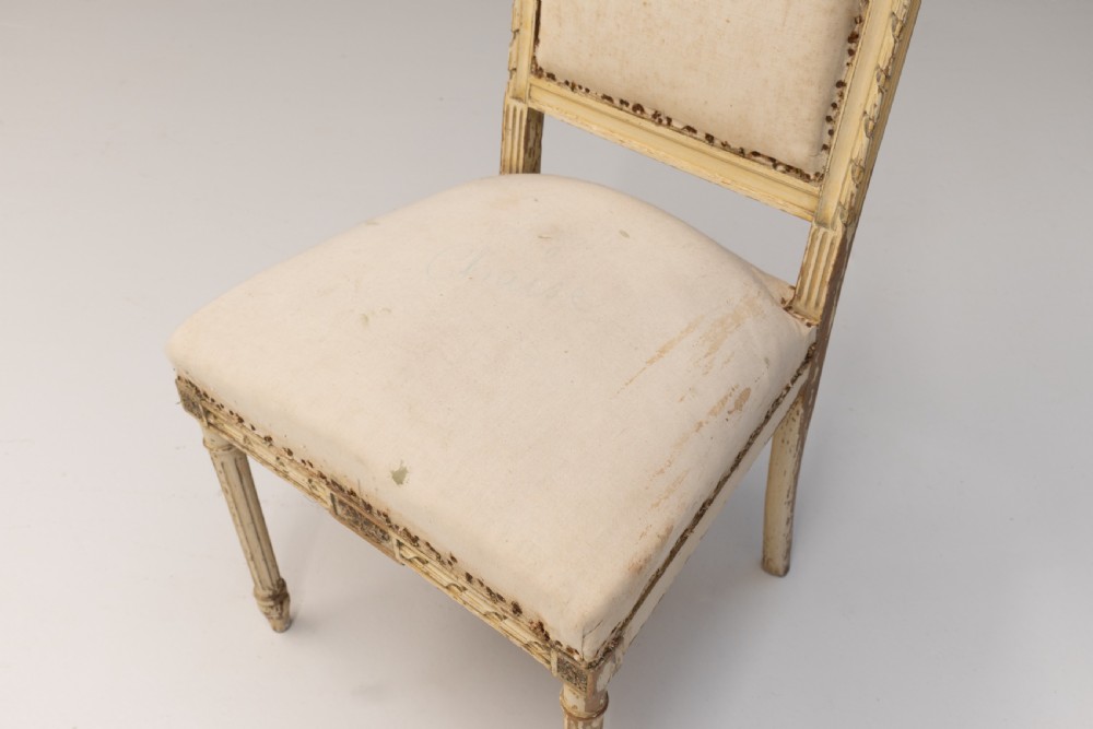 A pair of French Louis XVI style side chairs featuring distressed cream painted frames, tapered fluted legs, and neutral fabric upholstery. View VI