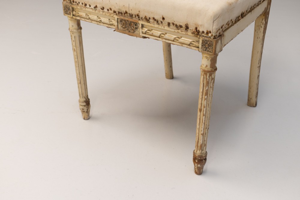 A pair of French Louis XVI style side chairs featuring distressed cream painted frames, tapered fluted legs, and neutral fabric upholstery. View VII