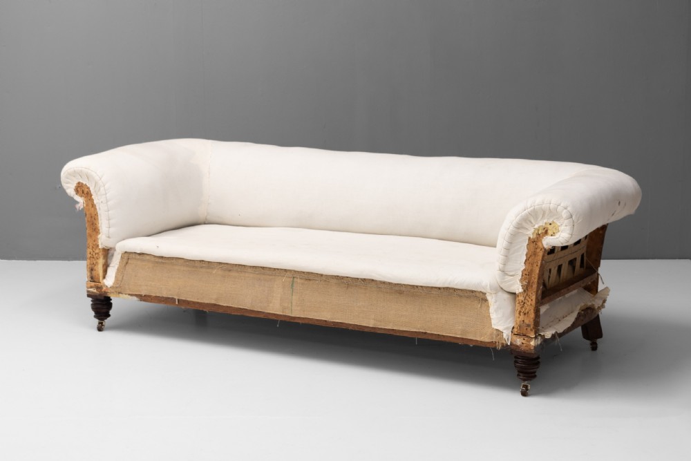 An antique Victorian Chesterfield settee upholstered in off-white calico lining, featuring deep rolled arms, exposed hessian lower upholstery, and turned mahogany legs with brass castors.