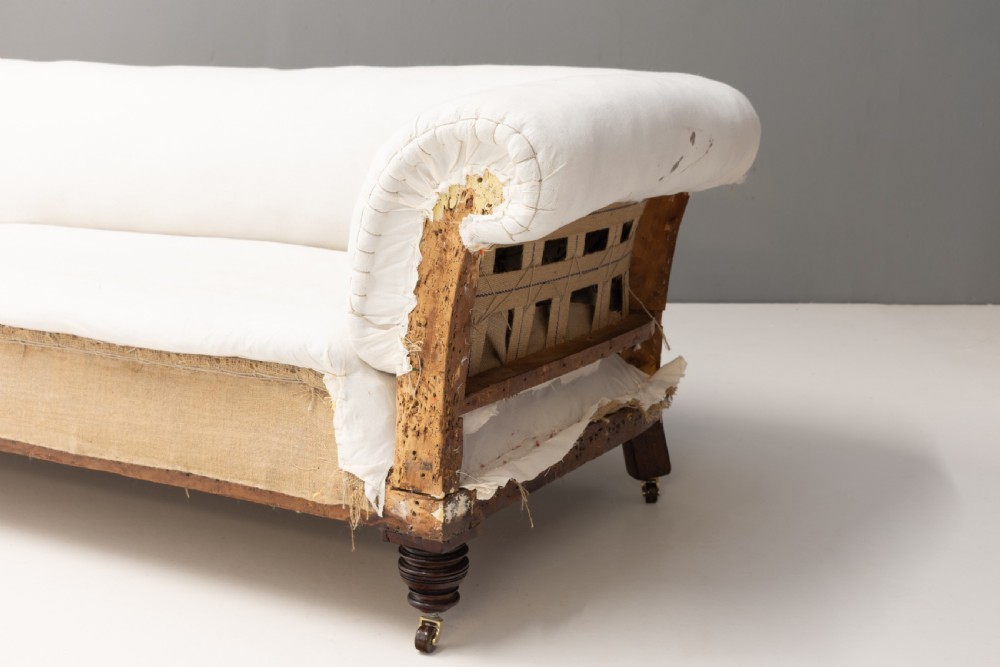 An antique Victorian Chesterfield settee upholstered in off-white calico lining, featuring deep rolled arms, exposed hessian lower upholstery, and turned mahogany legs with brass castors. View II
