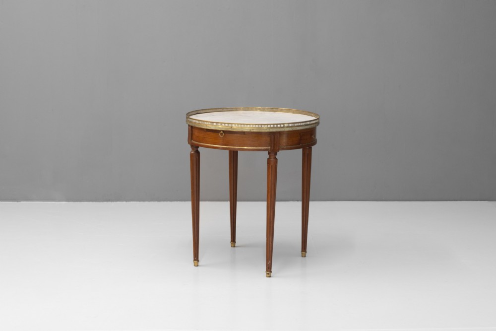 A circular Louis XVI style mahogany bouillotte table featuring a white marble top with a pierced brass gallery rim and fluted tapered legs.