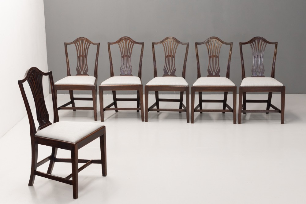 A set of six dark mahogany dining chairs featuring pierced splat backs, square stretchered legs, and light cream upholstered drop-in seats.