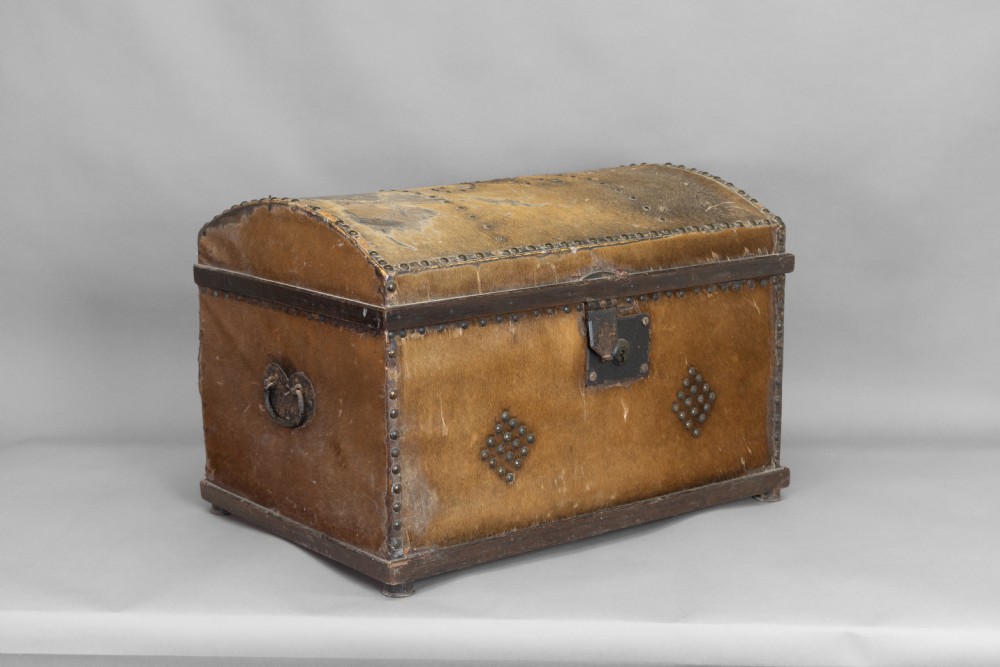 An antique domed-top storage trunk covered in natural brown hide, detailed with decorative iron studding and a central iron lockplate.