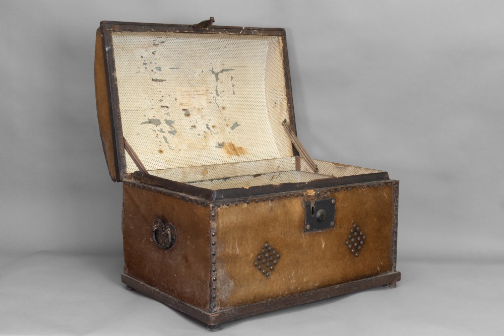 An antique domed-top storage trunk covered in natural brown hide, detailed with decorative iron studding and a central iron lockplate. View II