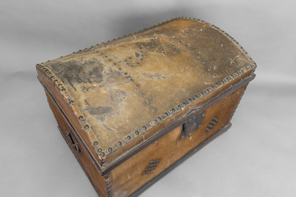 An antique domed-top storage trunk covered in natural brown hide, detailed with decorative iron studding and a central iron lockplate. View VII