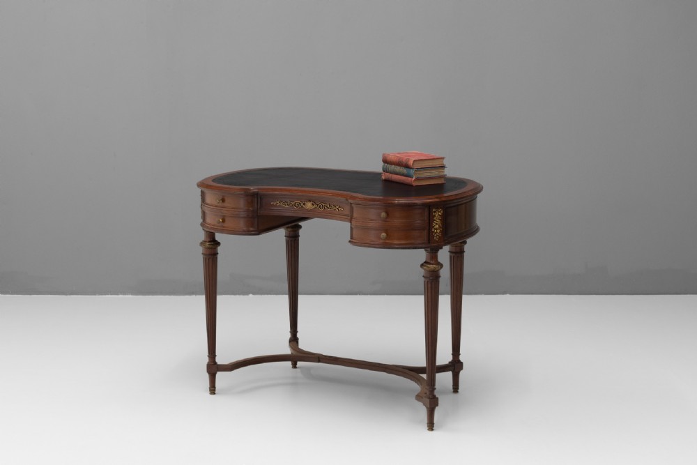 A mahogany kidney-shaped writing desk with a dark leather inset top, gilt-bronze mounts, four side drawers, and fluted legs joined by a curved stretcher. View II