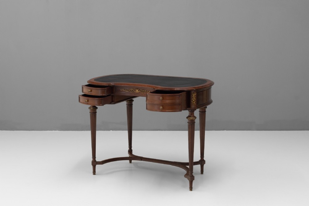 A mahogany kidney-shaped writing desk with a dark leather inset top, gilt-bronze mounts, four side drawers, and fluted legs joined by a curved stretcher. View III