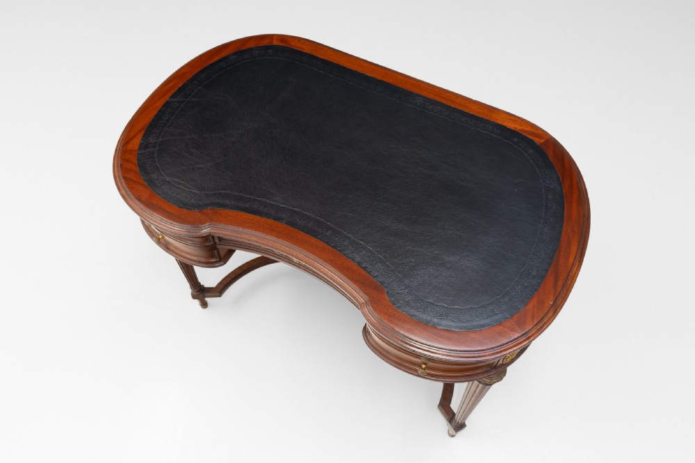 A mahogany kidney-shaped writing desk with a dark leather inset top, gilt-bronze mounts, four side drawers, and fluted legs joined by a curved stretcher. View IV