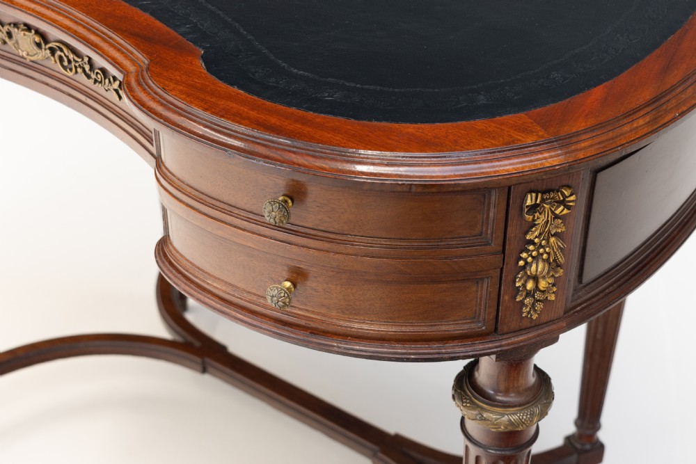 A mahogany kidney-shaped writing desk with a dark leather inset top, gilt-bronze mounts, four side drawers, and fluted legs joined by a curved stretcher. View V