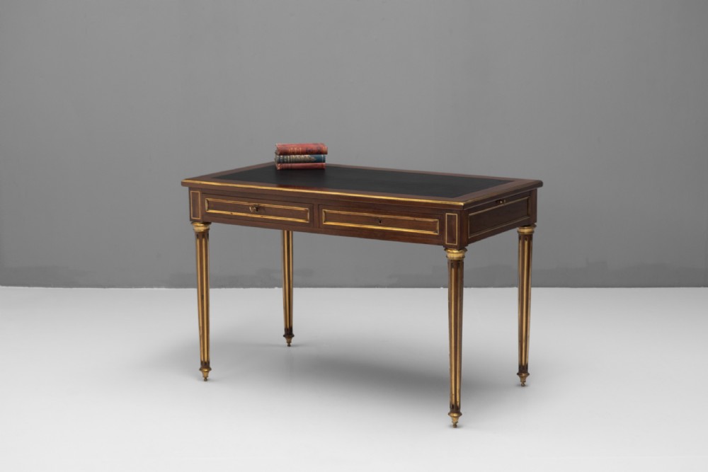 A French Louis XVI style mahogany bureau plat featuring a dark leather writing insert, gilt-bronze trim, frieze drawers, and fluted tapered legs. View IV